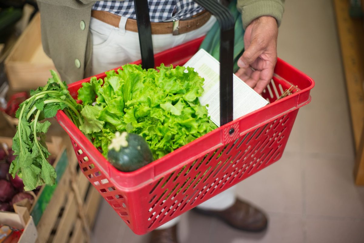 Panier de courses rouge rempli de salade et de légumes frais